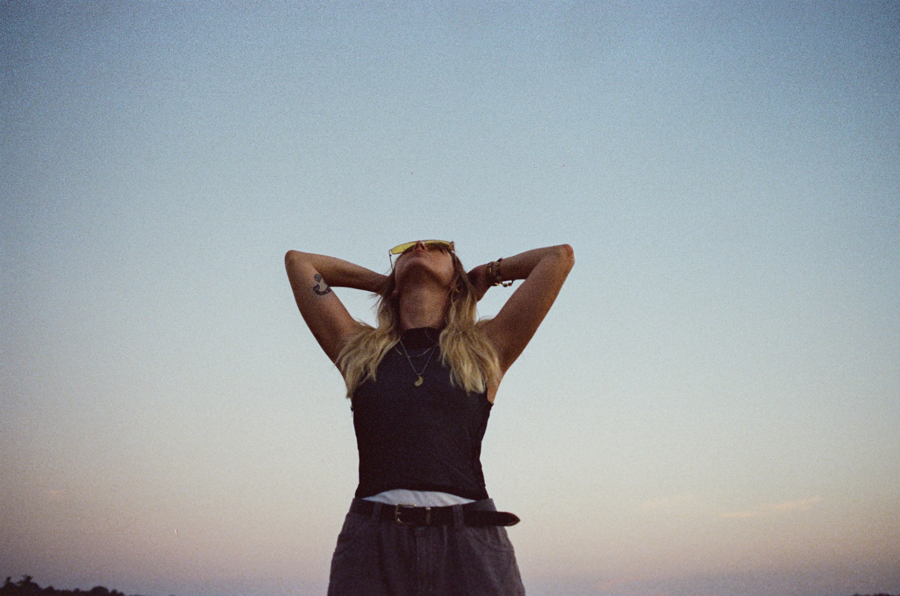 Original low-angle 35mm portrait of a woman with her head tilted back against a fading dusk sky